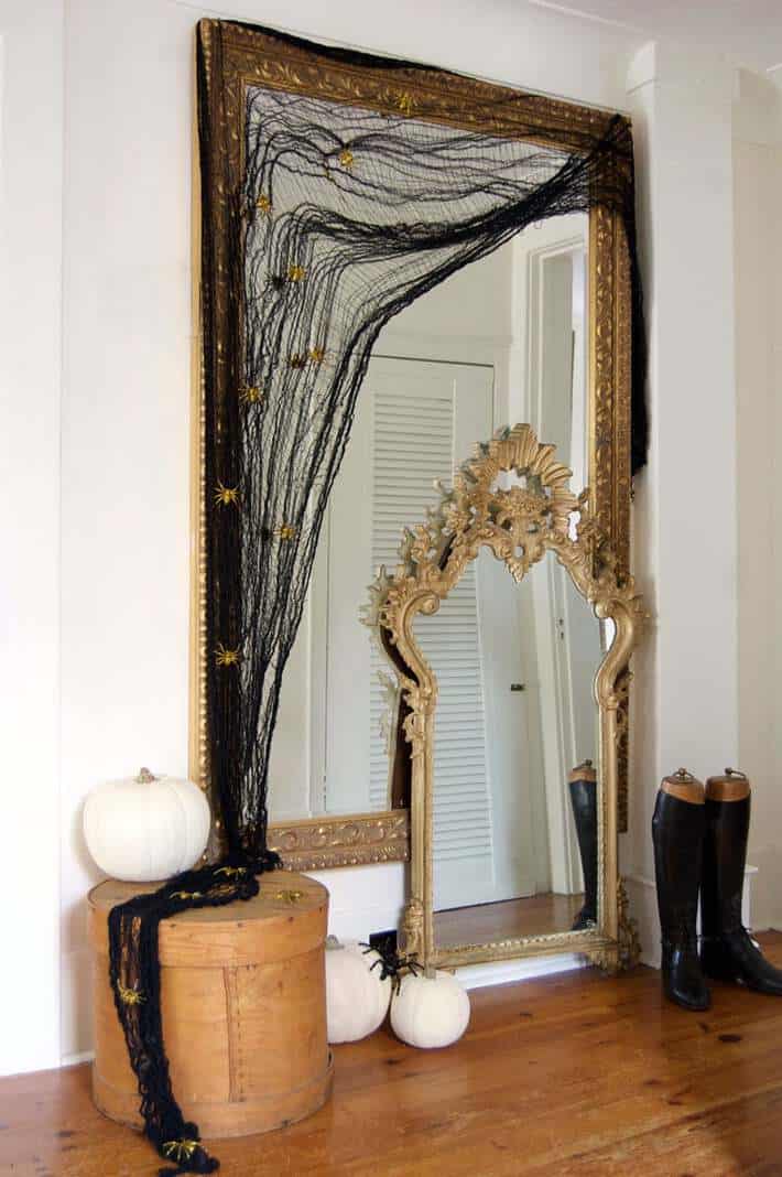 Black gauzy material swagged over large gold framed mirror, spilling on the floor below.