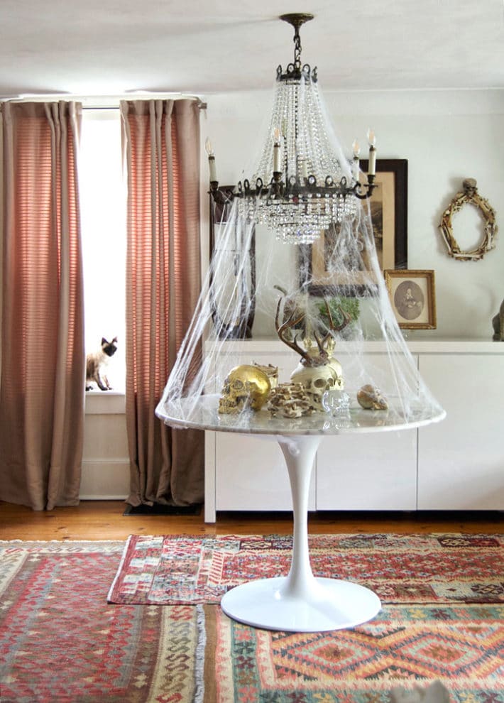 White marble tulip table covered in skulls beneath an antique chandelier covered in thin cobwebs for Halloween.