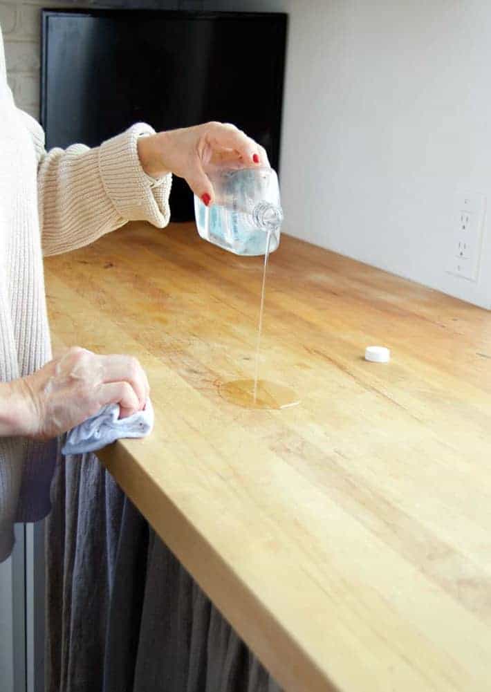 Drizzling mineral oil out of a bottle onto a wood countertop for maintenance.