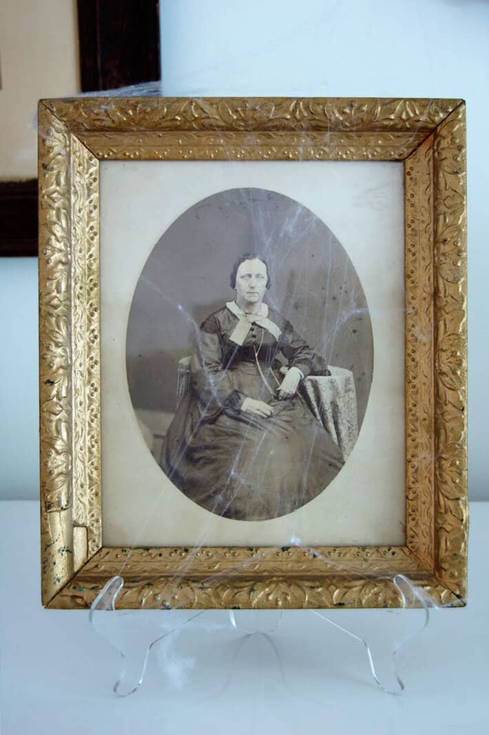 An antique portrait print from the 1800s in an ornate gold frame dripping with cobwebs.