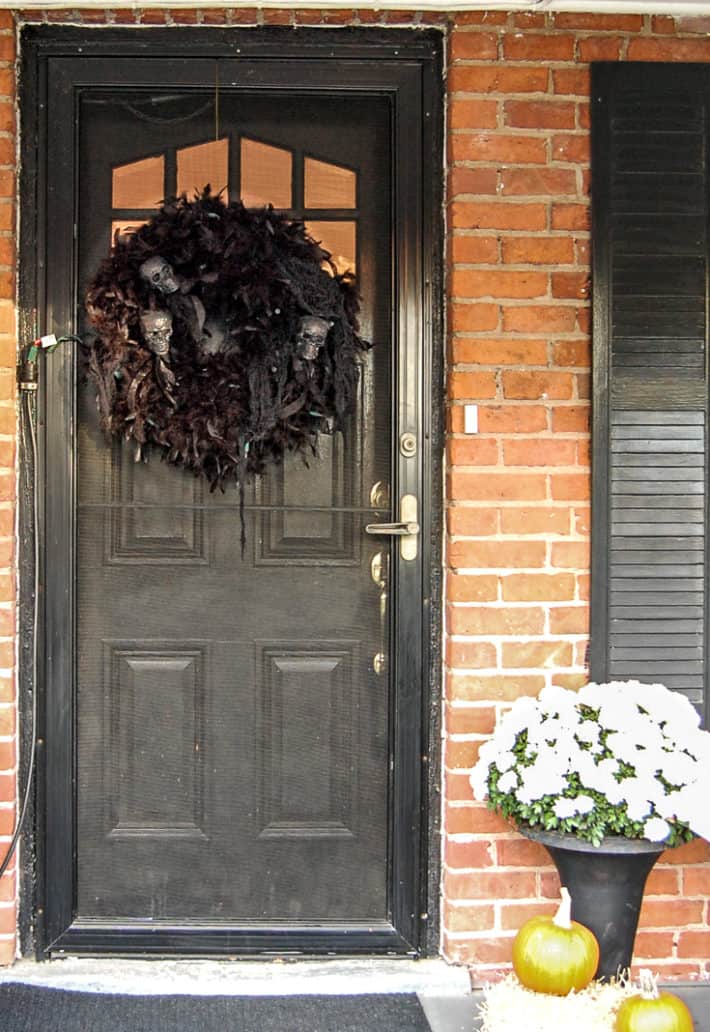 A Halloween wrath made of feather boas and skulls hangs from a black front door.