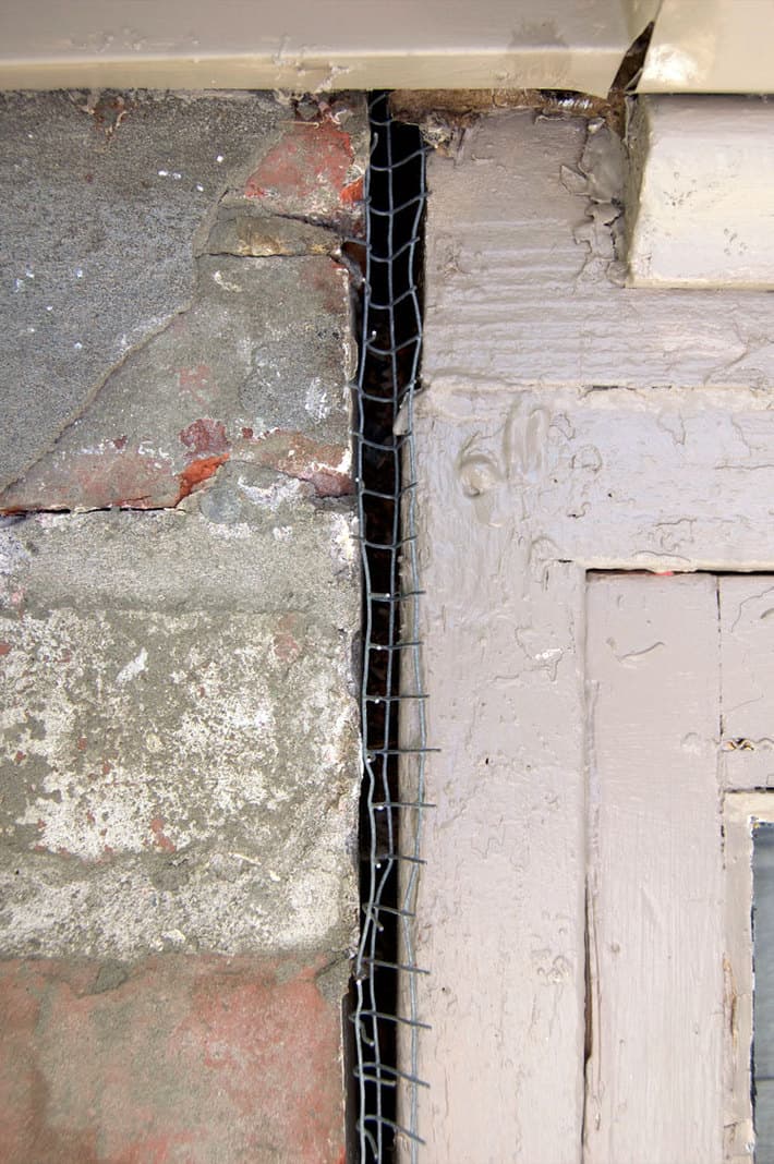 Hardware cloth squished into crack beside house bricks and wood window frame.