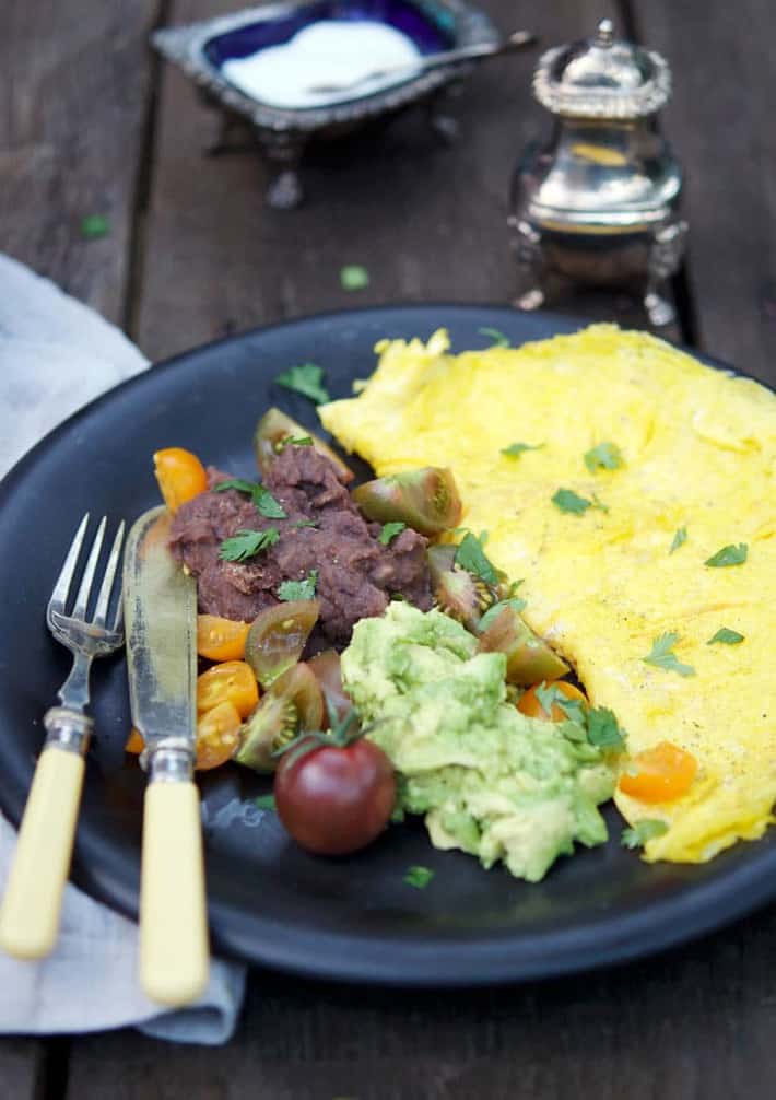 Thin omelette on a black plate with refried beans and avocado.