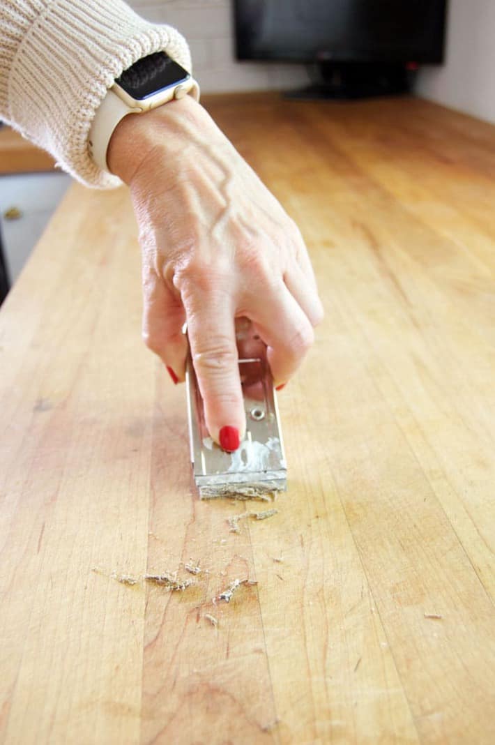 Running a paint scraper across a wood countertop to remove stuck flour. 