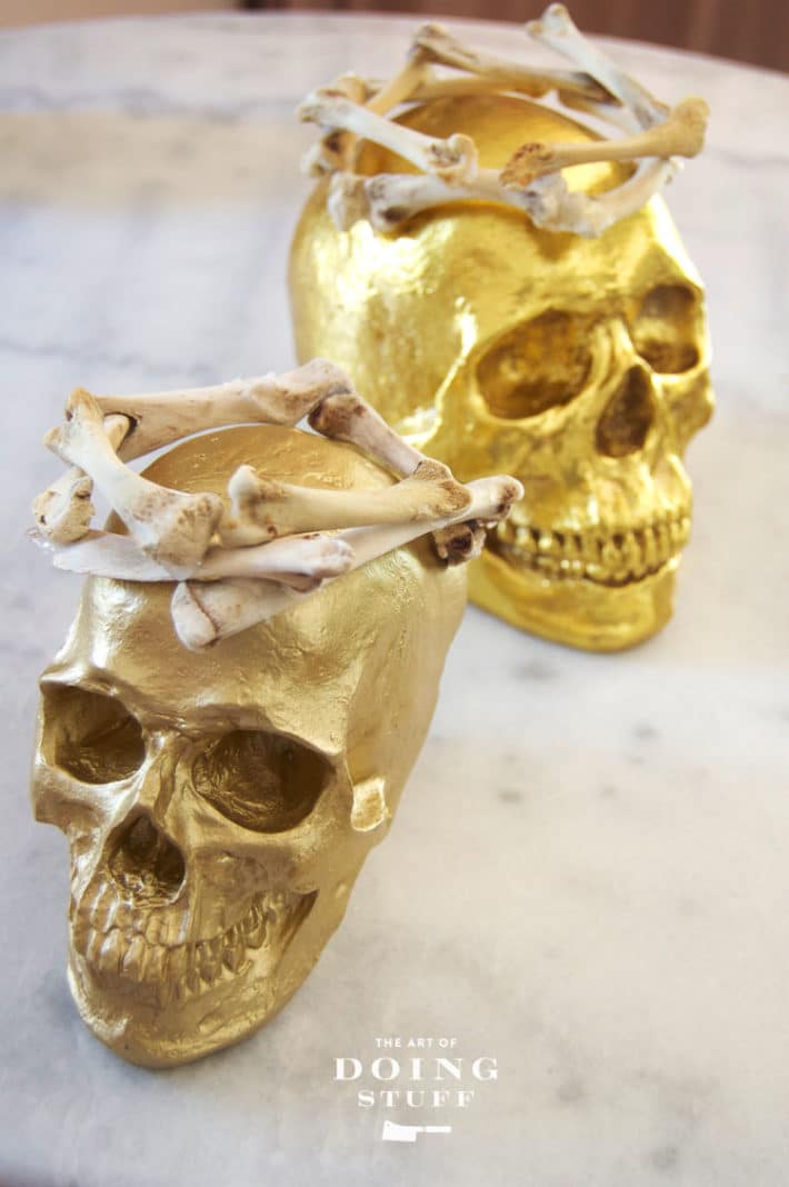 Weirdly elegant Halloween decorations of gold skulls with crowns on marble table.