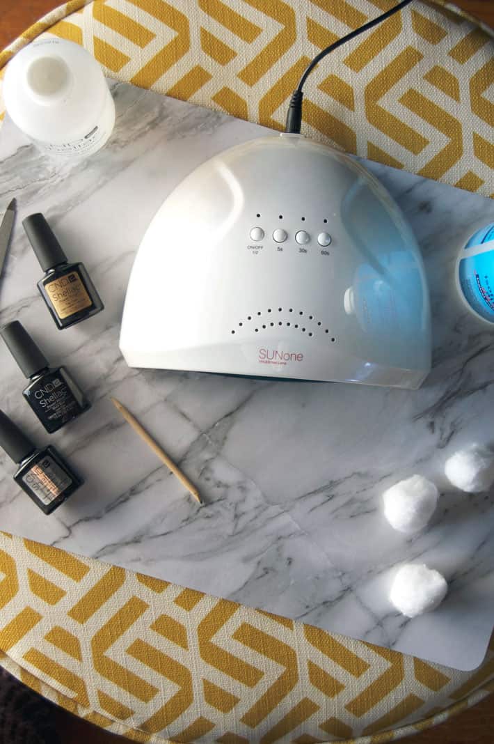 Overhead shot of an at home LED Nail lamp surrounded by polish, cotton balls and orange stick.