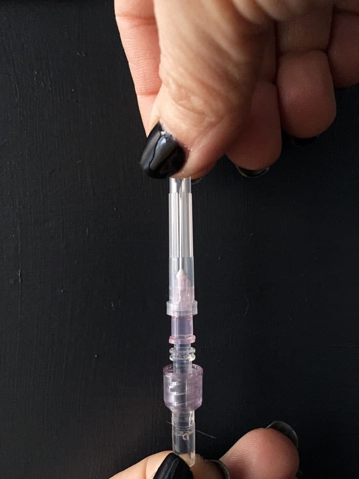 Removing the cap of an IV needle by carefully pulling it from the tip.