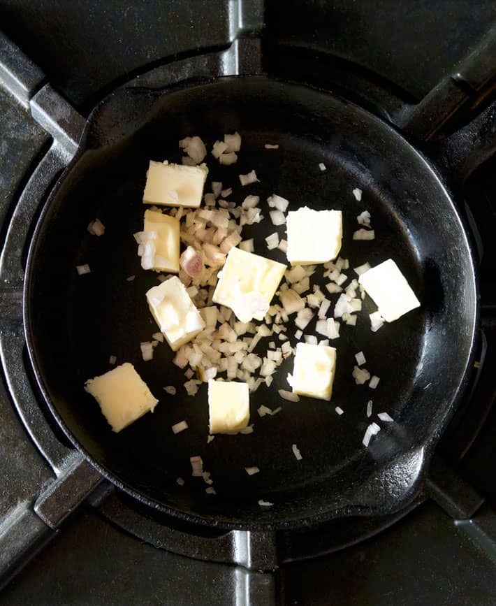 Cast iron pan on stove with chunks of butter and chopped shallot.