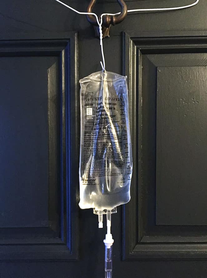 A subq fluids bag for cats hanging higher than the cat on a wire coat hanger on a black door.