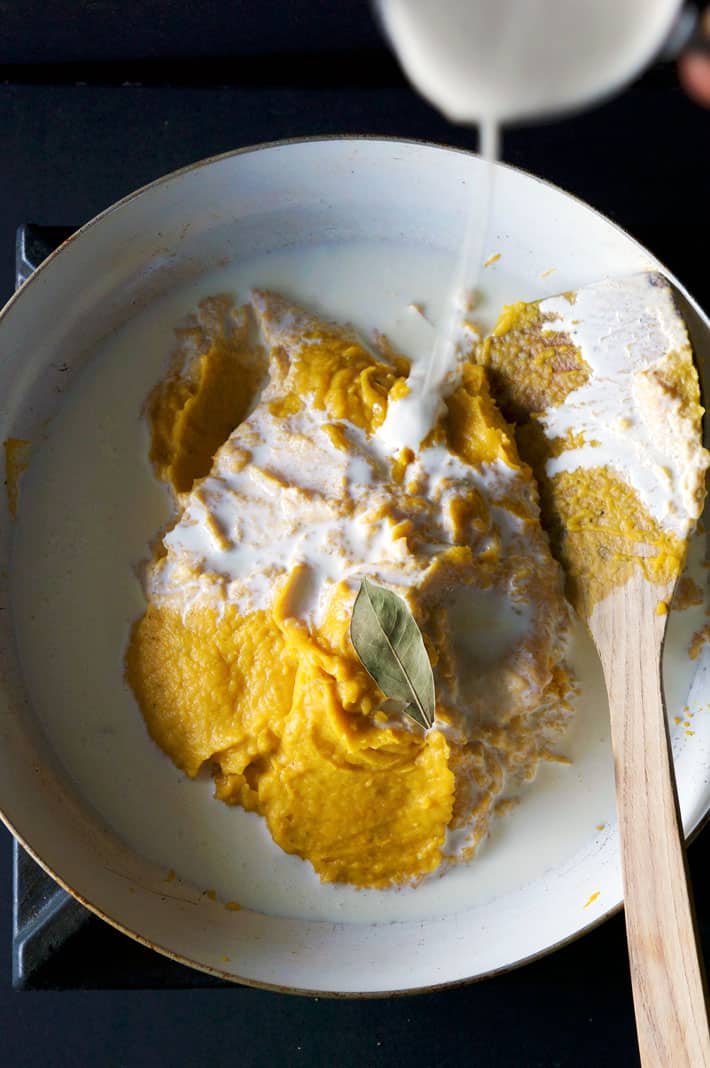 Pureed squash with bay leave and cream being added in non stick pan.
