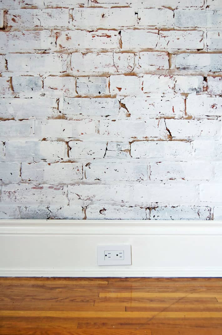 White painted brick wall with wide white baseboard and new white electrical outlet.