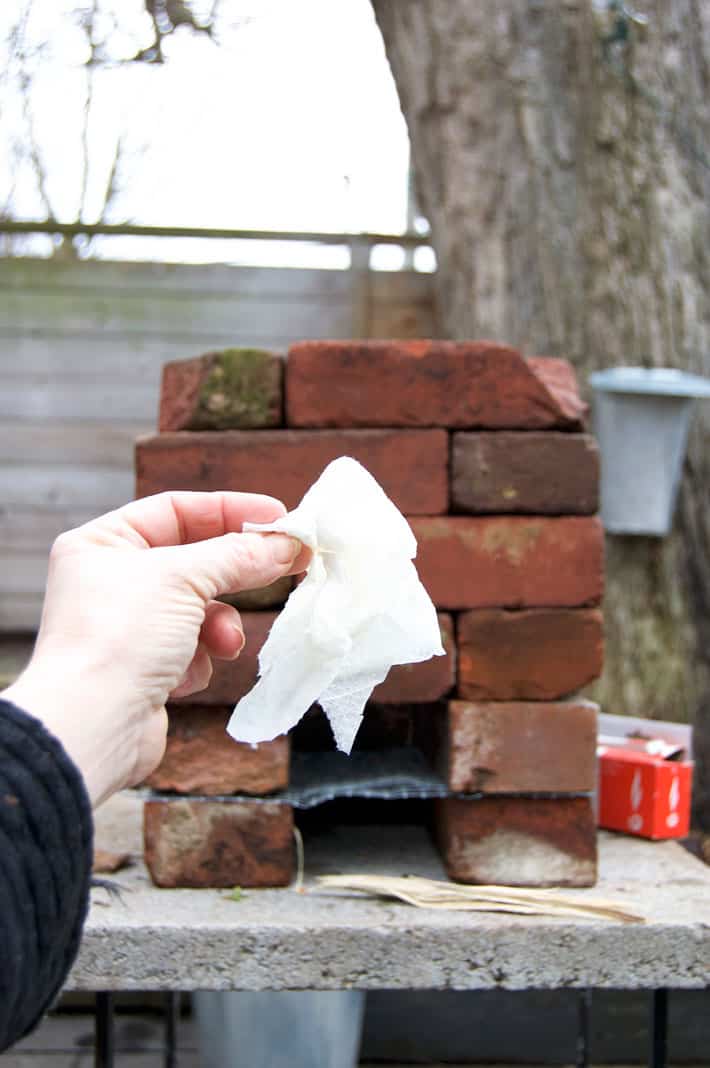 A vegetable oil soaked paper towel held up in front of a brick rocket stove outside.