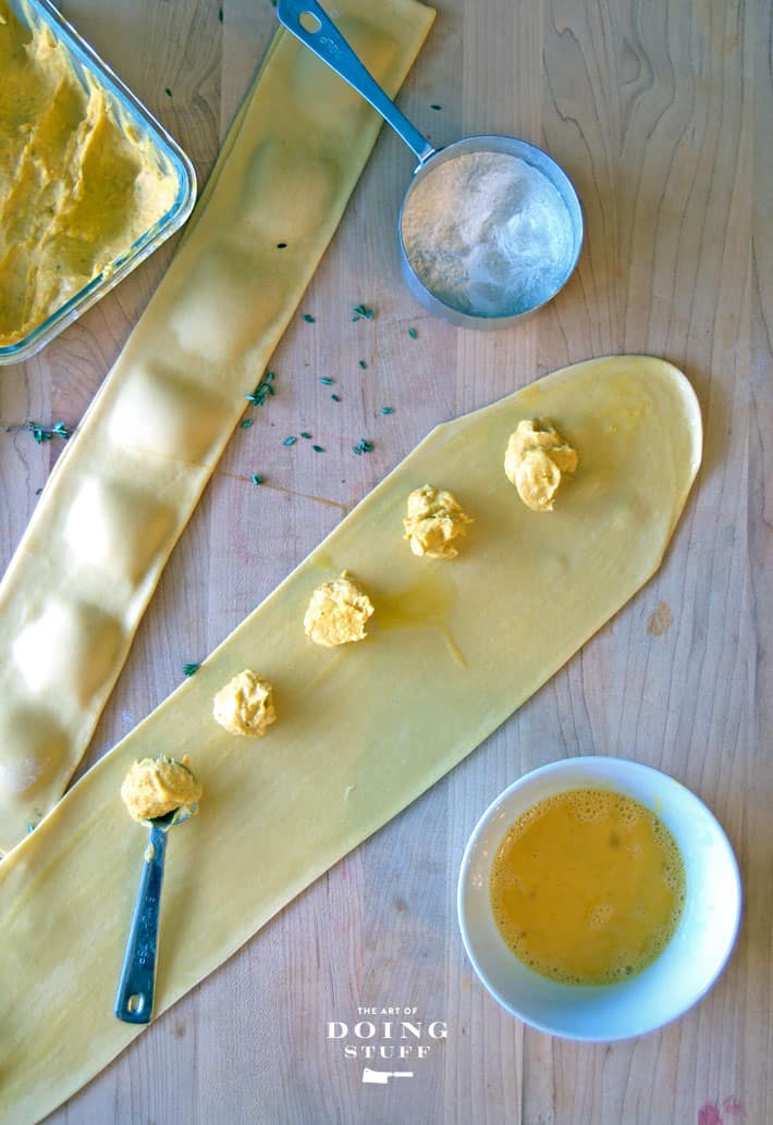 Overhead shot of strips of homemade pasta with pumpkin ravioli filling dotting the centre.