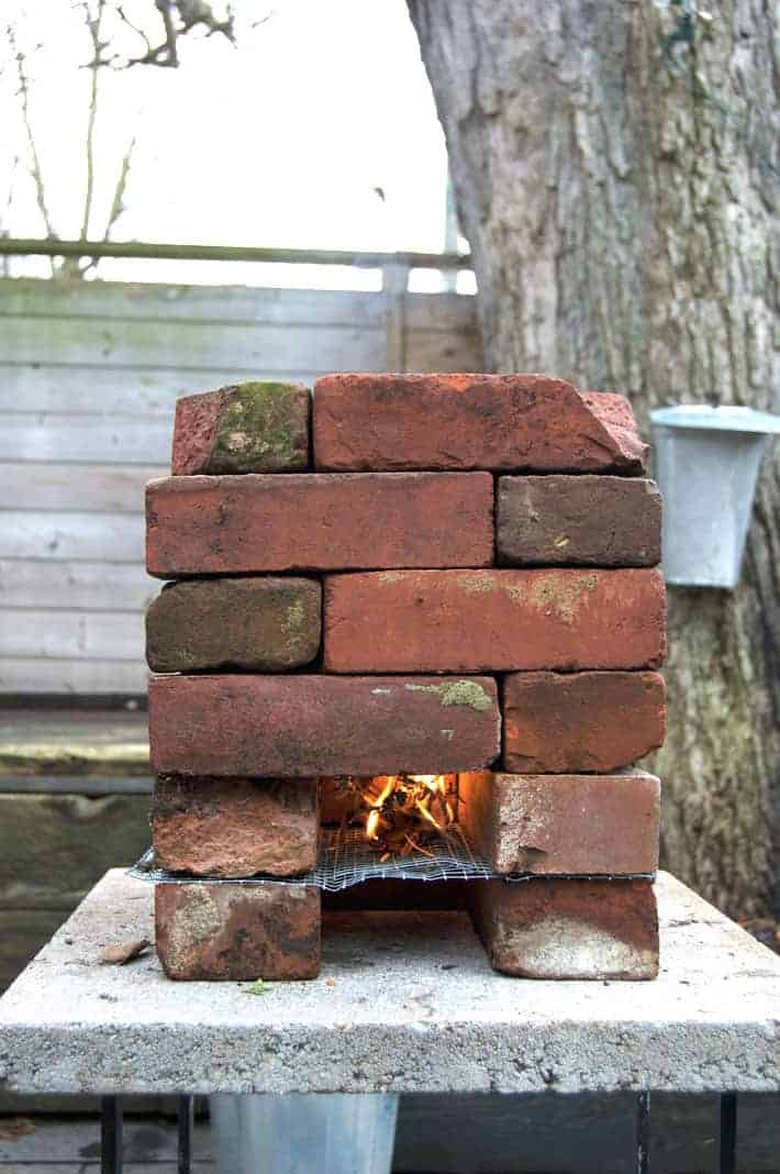 A lit DIY rocket stove sits on a backyard paver waiting to heat maple sap.