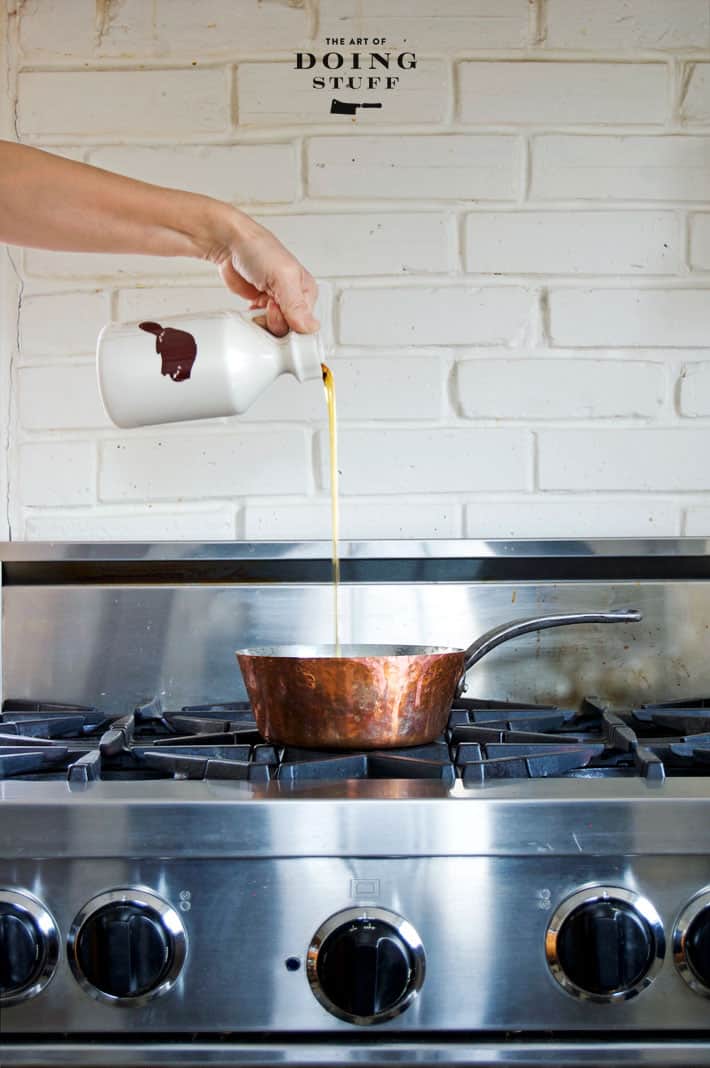 Pouring Maple Syrup into a copper pot sitting on a stainless steel range.