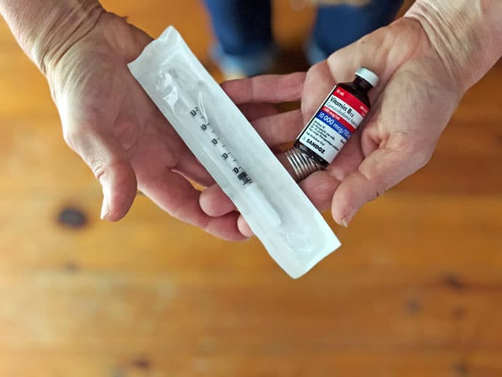 Hands holding a vial of vitamin B12 and syringe.