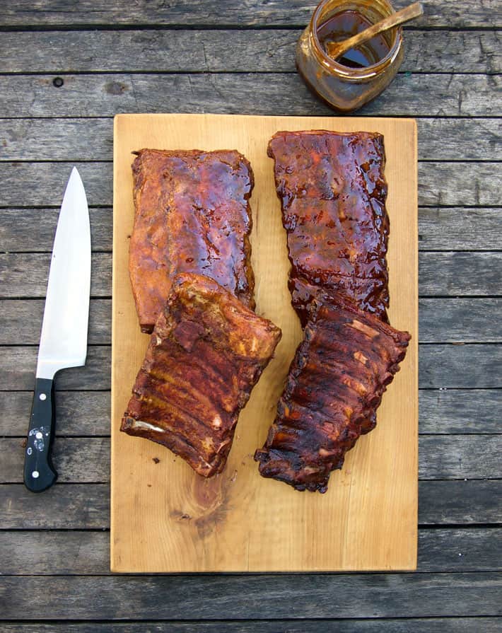 Beautiful racks of ribs on wood chopping block with knife and sauce to the side.