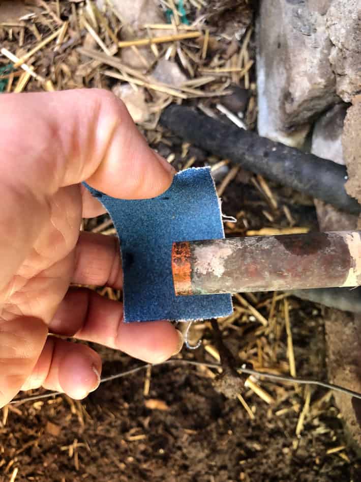 Sanding old copper pipe with blue sandpaper.