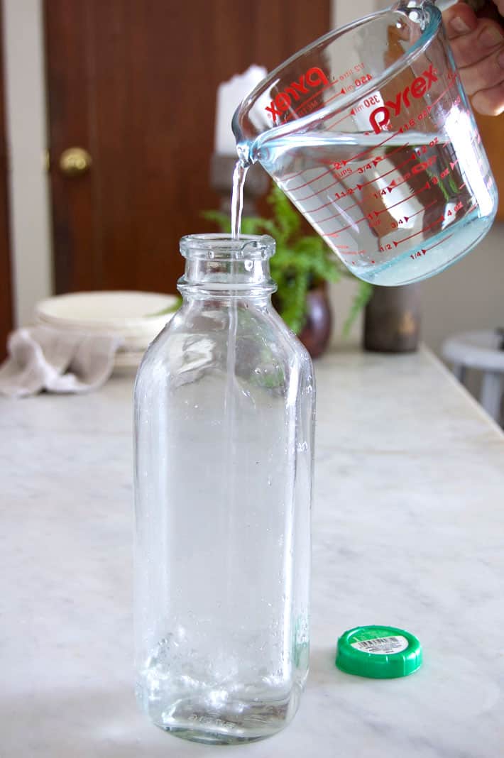 Pouring water from Pyrex measuring cup into clear glass milk bottle.