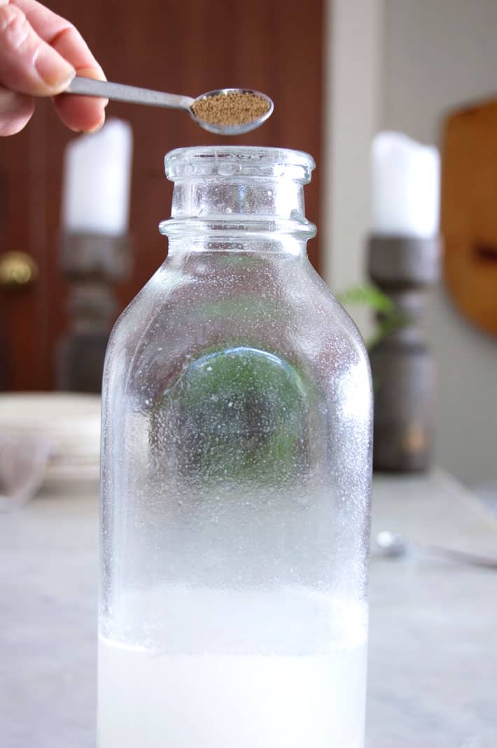 Pouring yeast grains from teaspoon into glass milk bottle.