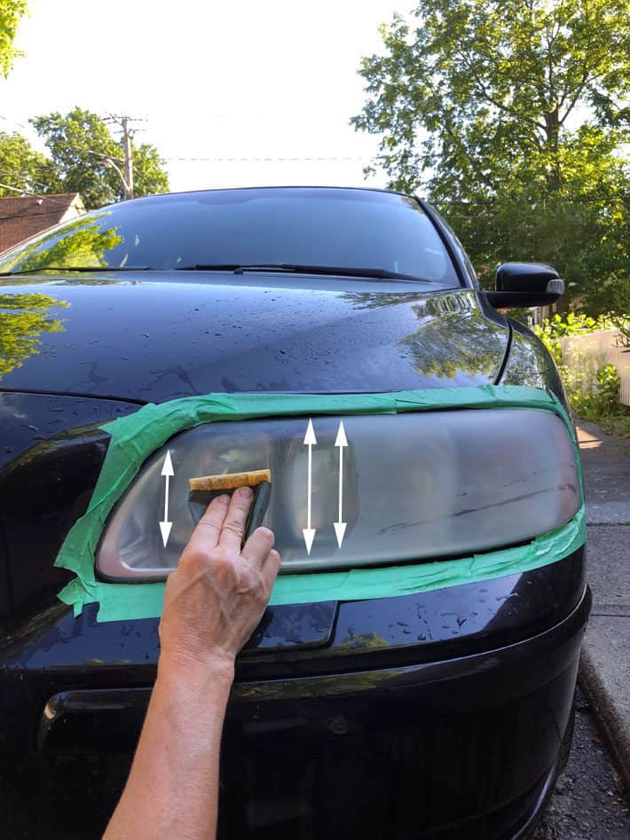 Sanding car headlight in a vertical motion using wet 1,500 grit sandpaper.