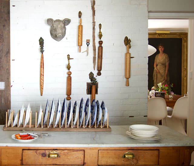 DIY plate rack filled with flow blue china, set on antique marble kitchen island in front of white painted brick wall.