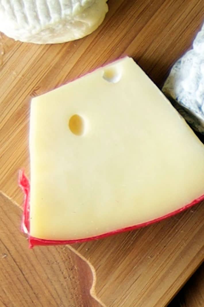 7 of the tastiest cheese options for your burger. View of red wax encased fontina cheese, which is perfect for a burger because of how well it melts.