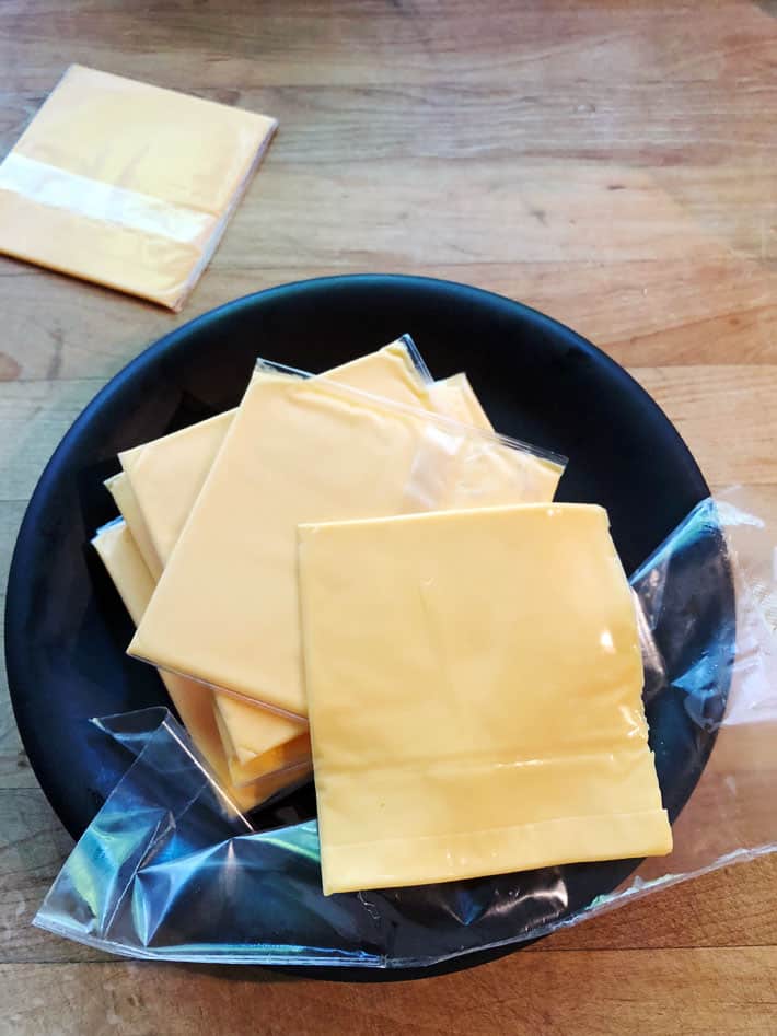 7 of the tastiest cheese options for your burger. Stack of the classic plastic wrapped cheese on a black plate.