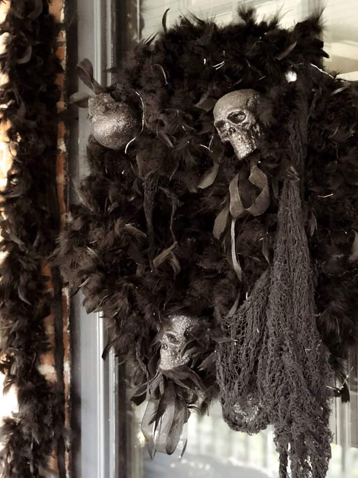 A Halloween wrath made of feather boas and skulls hangs from a black front door.