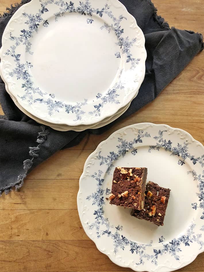 Two chocolatey, nut covered weed brownies on a blue and white transferware plate.