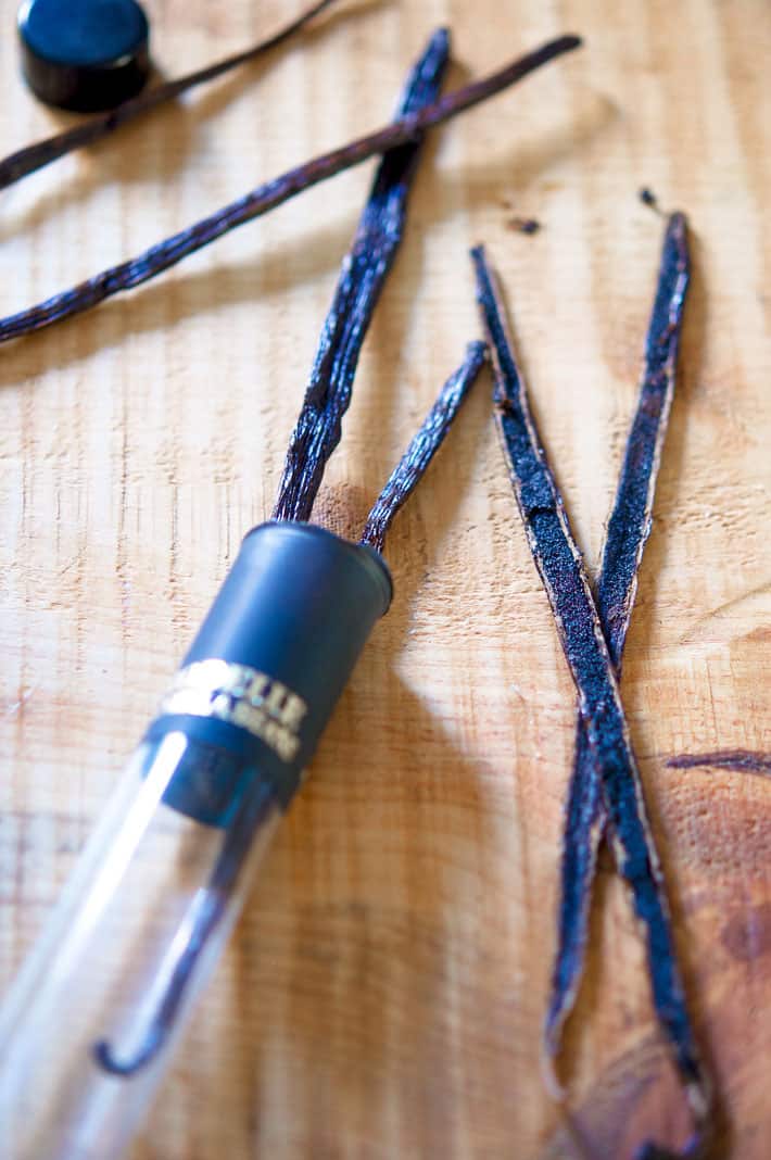 Vanilla beans split down the centre to expose the seeds laid on a wood cutting board.