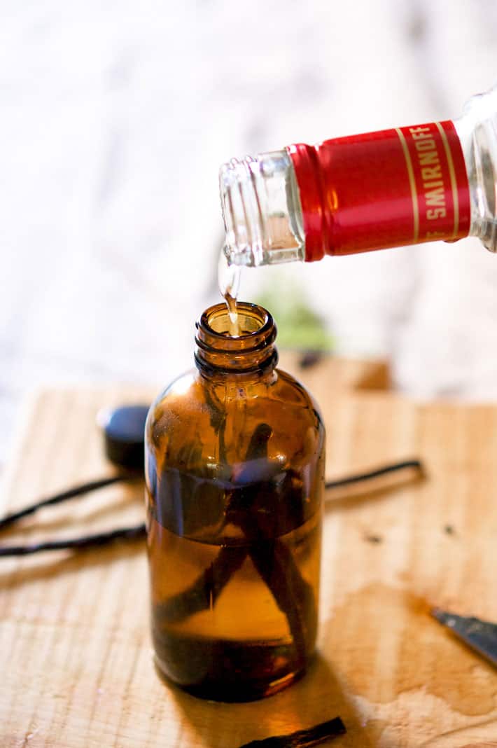 Vodka being poured into an amber glass bottle with a couple of vanilla beans in it.