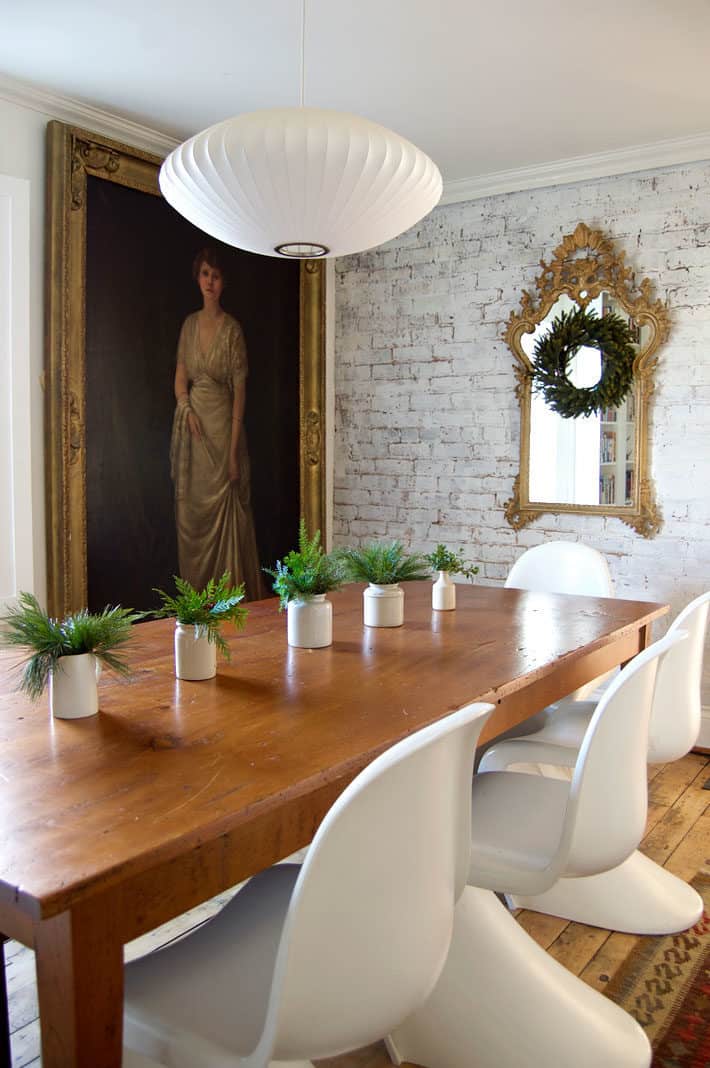 Antique brick wall painted white in dining room with harvest table and white Panton S chairs.