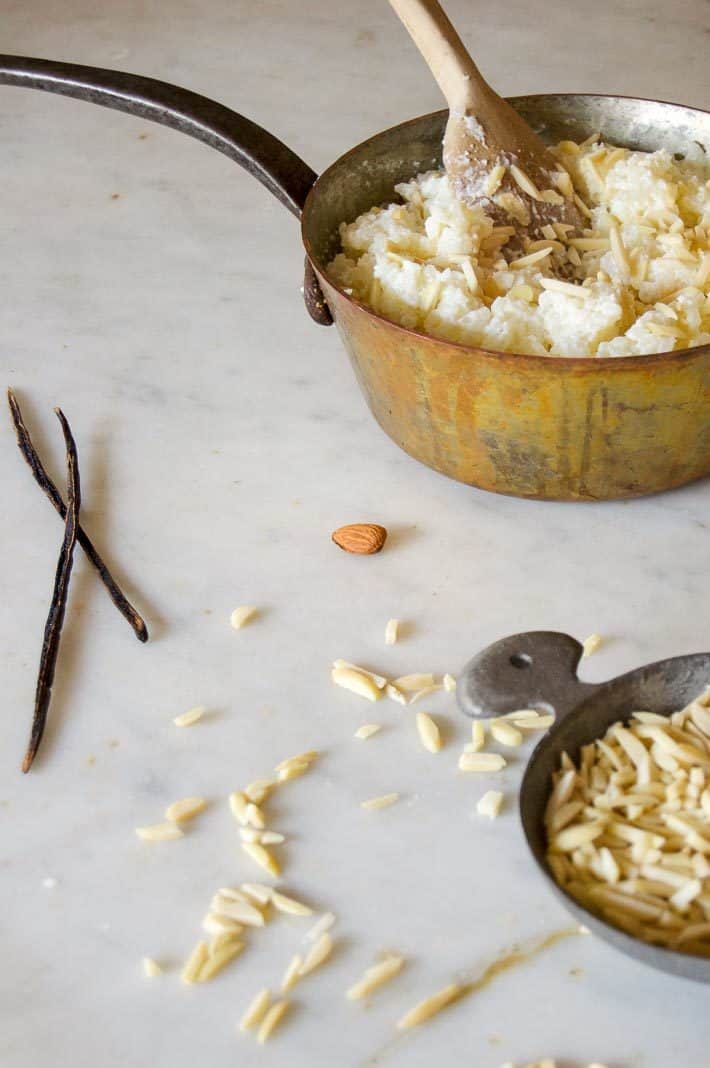 Danish rice pudding topped with slivered almonds in a copper pot on a marble countertop. 