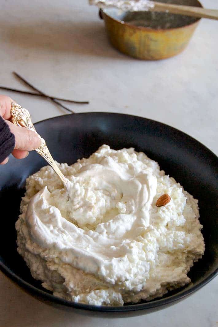 Stirring whipped cream into delicious rice pudding in a large black bowl with a gold spoon.