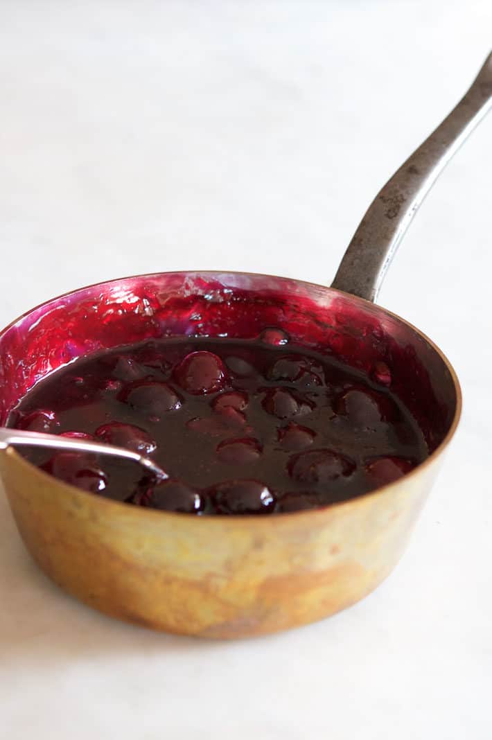 Cherry sauce cooling in a copper pot on a marble countertop.