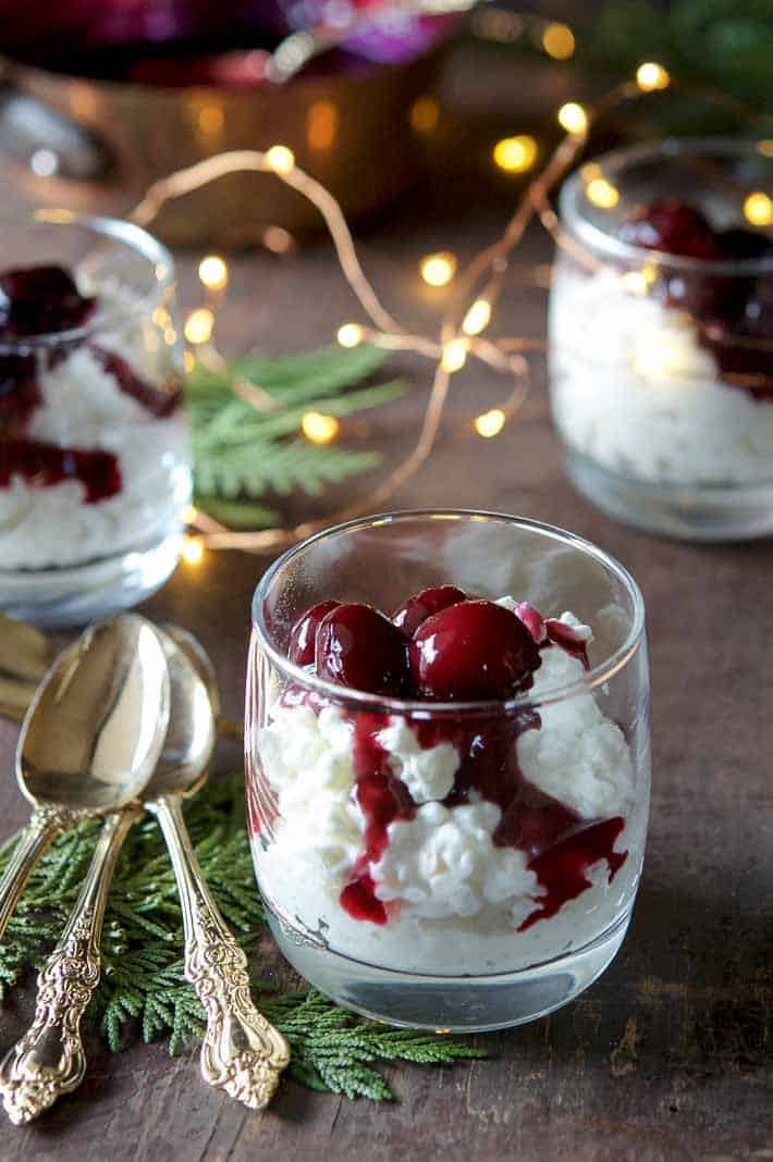Risalamande in a clear glass with cherries and sauce dripping into the pudding.