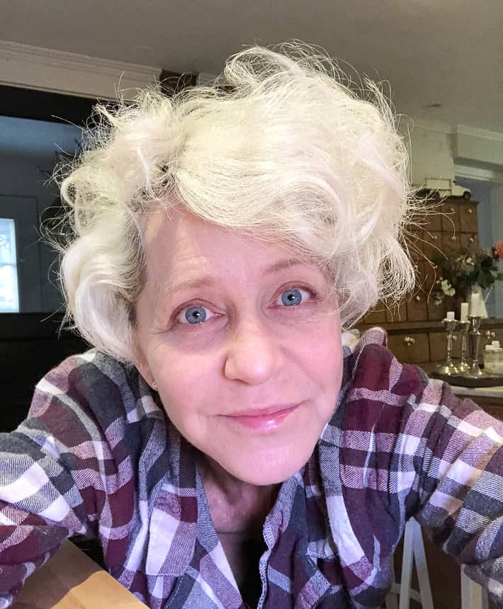 A photo of Karen, who is wearing a purple and gray checked shirt, after curling her short, blonde hair to emulate Charlize Theron. 