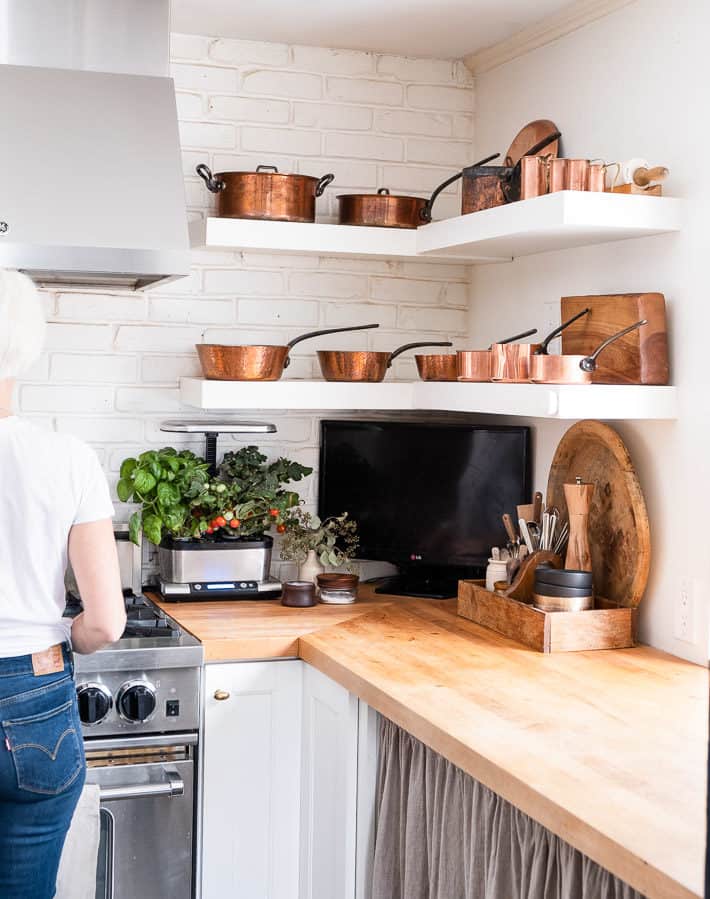 Maple butcher block counters glow with 2 floating shelves of gleaming copper pots hanging above.