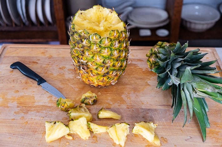 Pineapple and pieces of pineapple on wood cutting board.