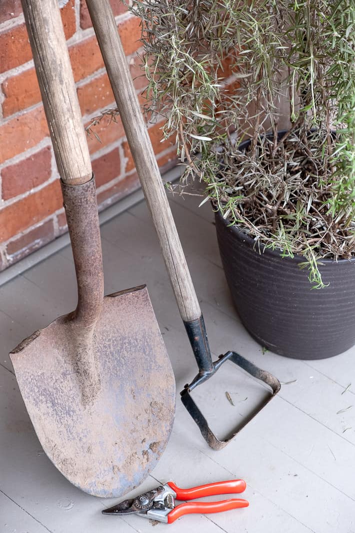 How to maintain your garden tools. Trio of garden tools leaning against a brick wall before receiving routine maintenance like cleaning, sharpening and oiling.