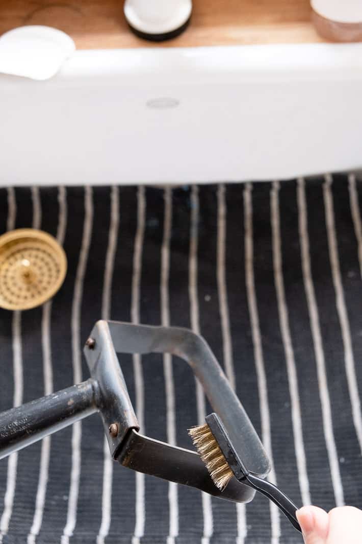 Garden stirrup hoe, also called a loop hoe, being cleaned in white enamel kitchen sink with a wire brush.