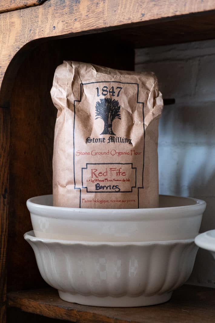 How to grow and harvest wheat on a small scale. A paper bag of Red Fife Wheat berries from 1847 Stone Milling sits in an ironstone bowl.
