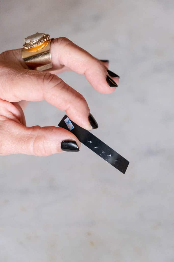 Woman's fingers with black nail polish and gold ring, holding a black Dymo label that hasn't printed properly.