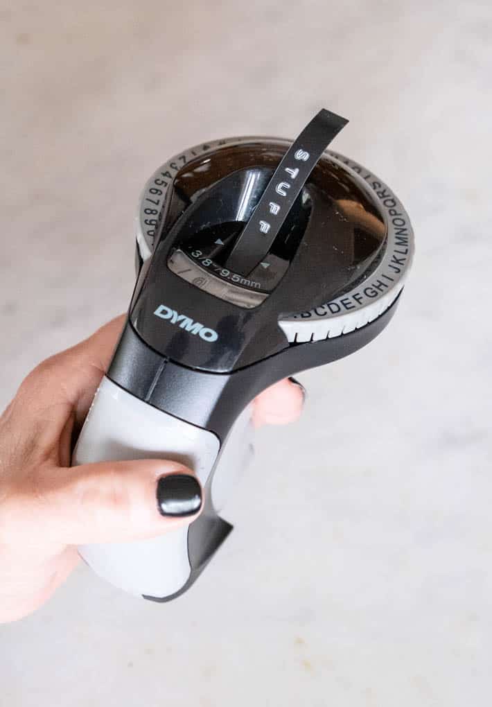 Dymo Organizer Xpress label maker being held over a marble counter, with the word "STUFF" printed out neatly from the device.