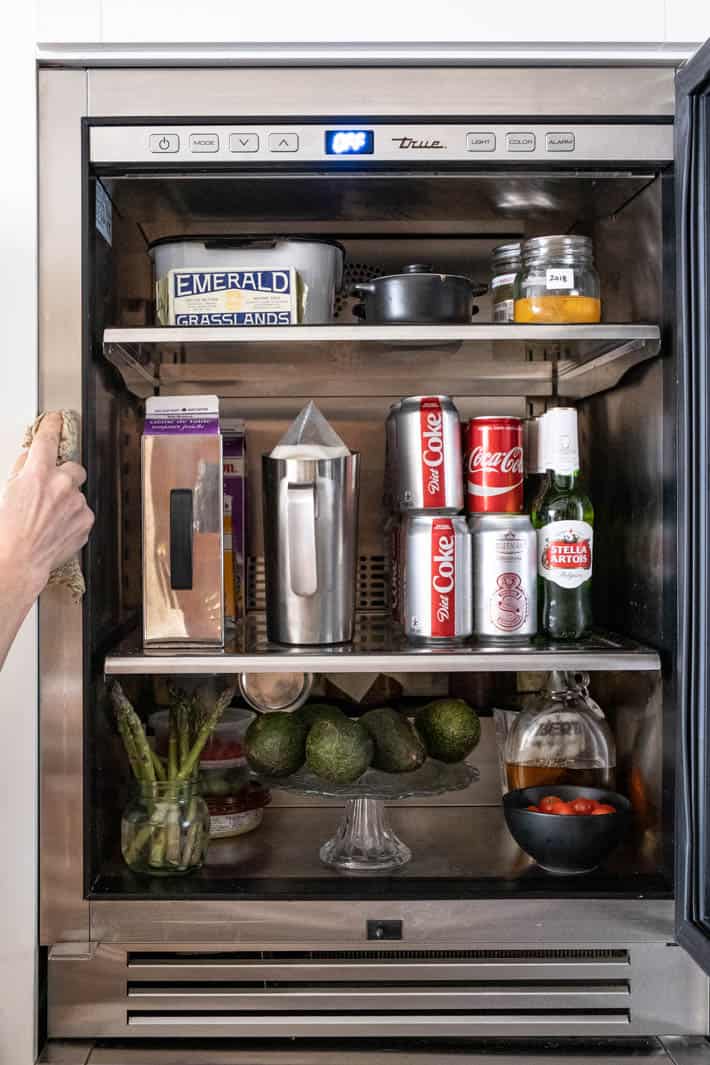 Cleaning the edge of a stainless refrigerator where the gasket hits it, contents of the fridge like butter, milk and avocados visible.