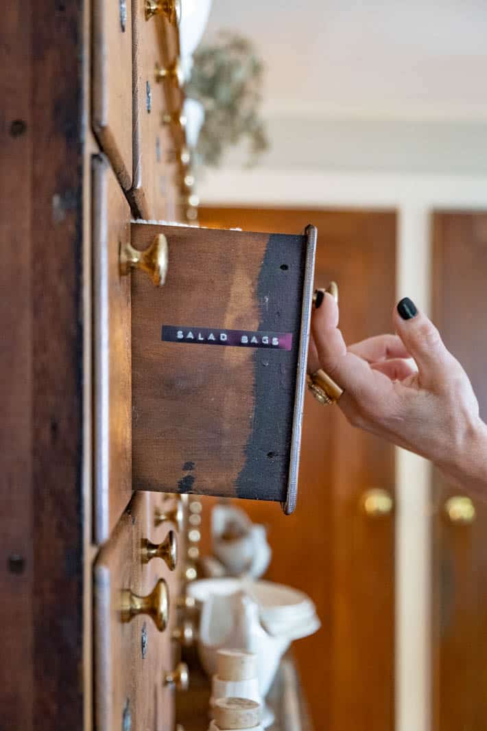 Antique wood apothecary drawer being pulled out shows a label on the side of the drawer outlining the contents of it. 