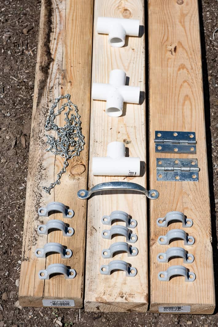 Some of the hardware needed to build a hinged hoop house set on 2x4s including conduit clamps, a handle, hinges, pvc connectors and chain.