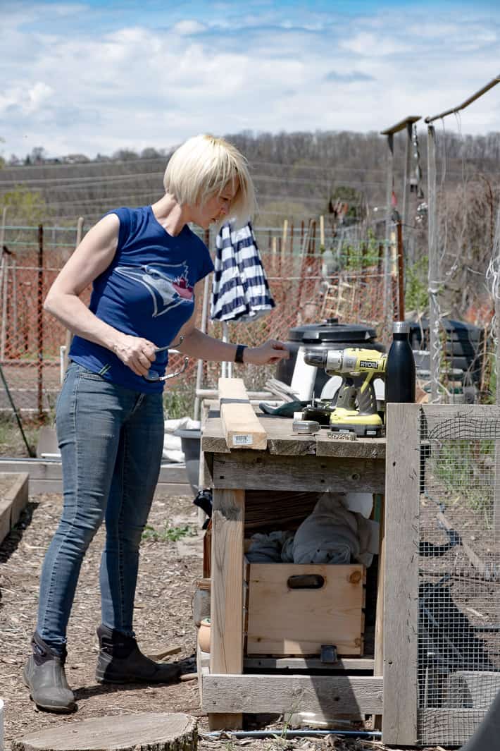 Karen Bertelsen assesses her tools laid out on a garden potting bench before building a hinged hoop house. Blue skies seen in the background.