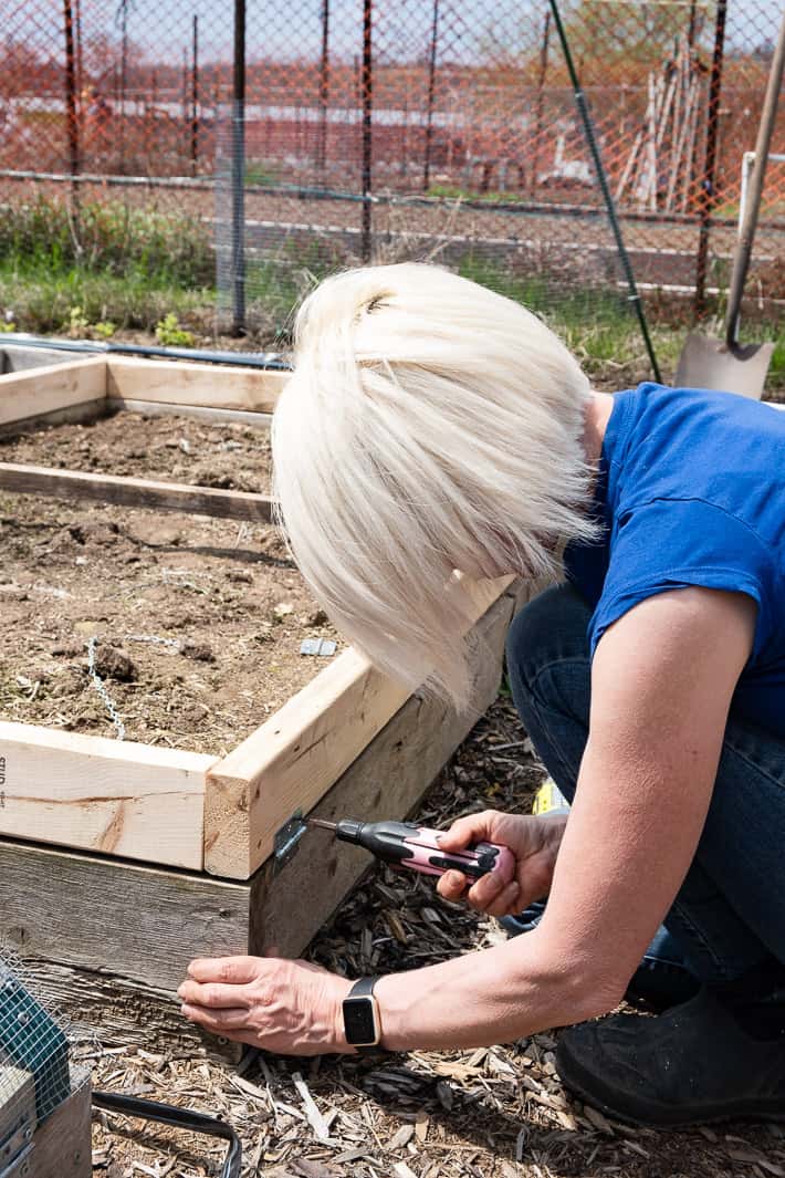 Karen Bertelsen screws hinges into the long end of a hoop house frame to allow it to open and close.